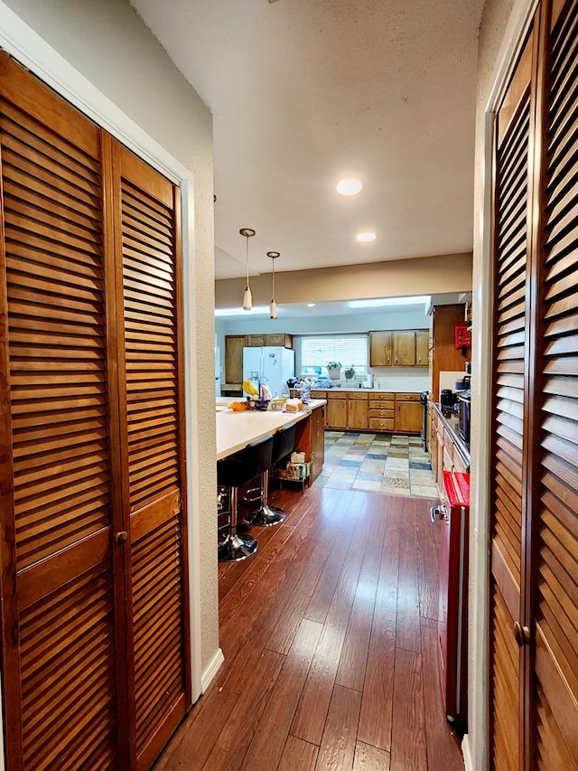 kitchen with brown cabinetry, freestanding refrigerator, dark wood-type flooring, light countertops, and decorative light fixtures
