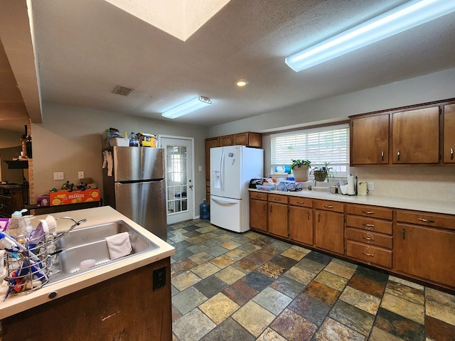 kitchen featuring white refrigerator with ice dispenser, a sink, light countertops, freestanding refrigerator, and stone tile flooring