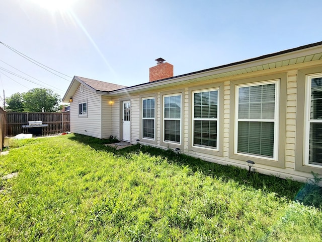 back of property with fence, a chimney, and a lawn
