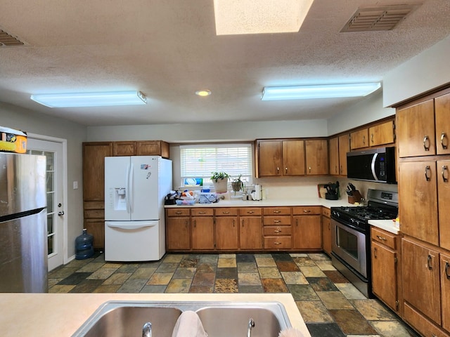 kitchen featuring brown cabinetry, visible vents, light countertops, a sink, and stainless steel appliances