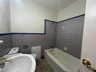 bathroom featuring a sink, tile patterned floors, toilet, and tile walls