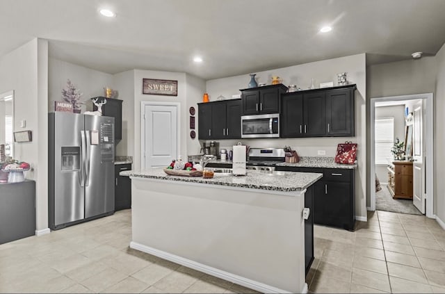 7018 Adenium Rd, Odessa, TX 79765 - kitchen with appliances with stainless steel finishes, dark cabinets, a kitchen island with sink, light tile patterned floors, and light stone counters