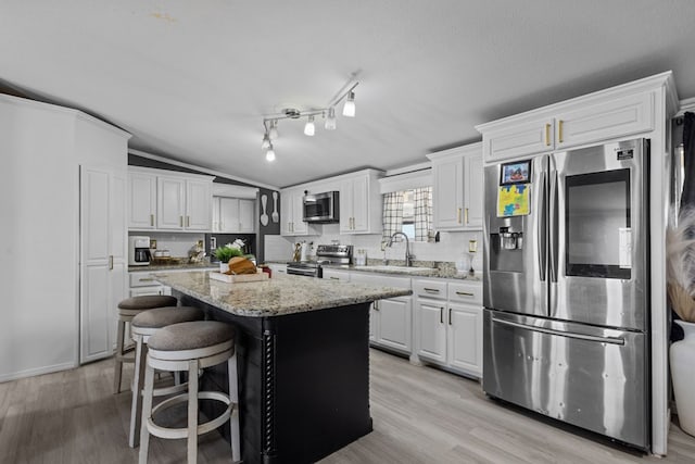 kitchen with light wood-style flooring, stainless steel appliances, a sink, white cabinets, and vaulted ceiling