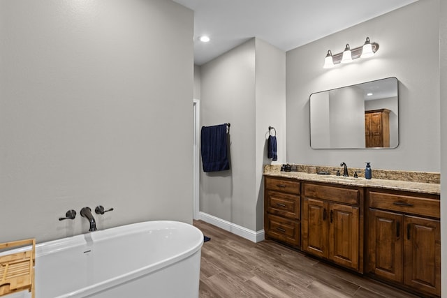 full bathroom featuring wood finished floors, vanity, a soaking tub, recessed lighting, and baseboards