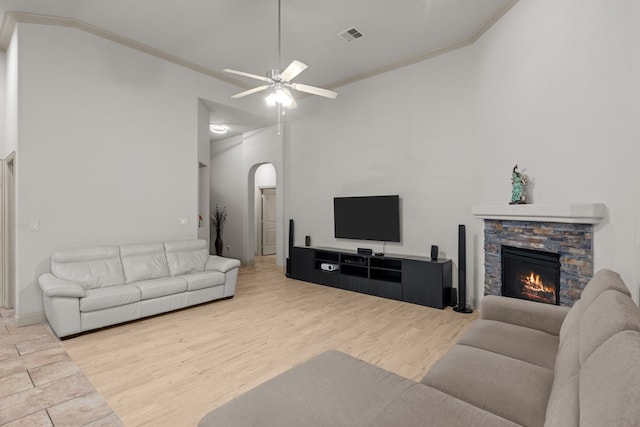 living room with wood finished floors, a fireplace, crown molding, ceiling fan, and arched walkways