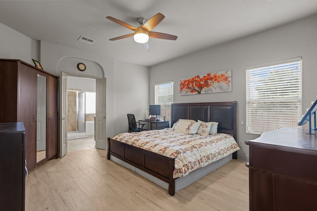 bedroom with ensuite bath, visible vents, light wood finished floors, ceiling fan, and baseboards
