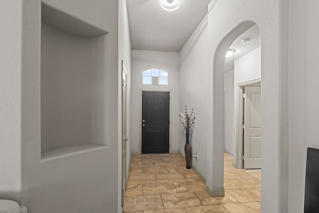 doorway to outside with baseboards, stone finish floor, and arched walkways