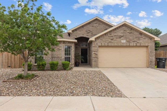 view of front of home featuring driveway, brick siding, an attached garage, and fence