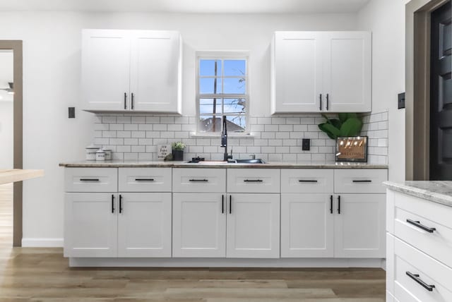 kitchen featuring backsplash, light wood-type flooring, a sink, light stone counters, and white cabinetry