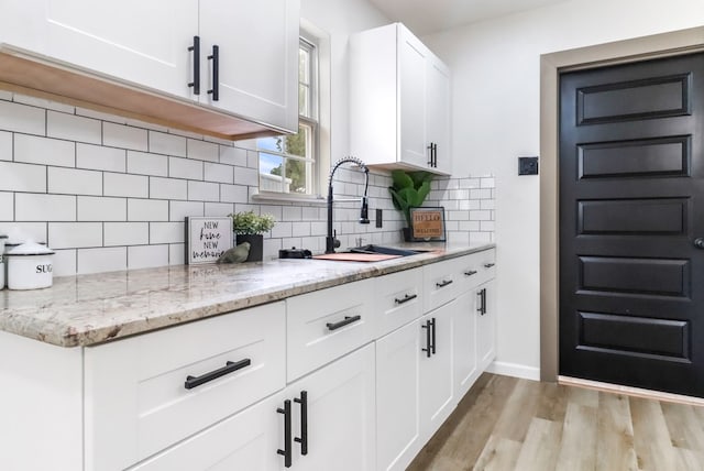 kitchen with white cabinets, light stone counters, a sink, light wood-style floors, and backsplash