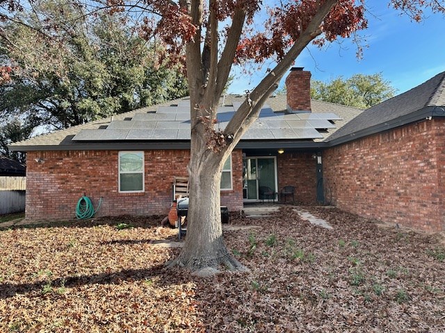 1203 S Nelson Ave, Monahans, TX 79756 - rear view of house featuring a chimney, solar panels, brick siding, and roof with shingles
