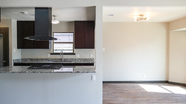 4603 N Tom Green Ave, Odessa, TX 79762 - kitchen with island exhaust hood, black stovetop, light wood finished floors, dark stone countertops, and dark brown cabinets