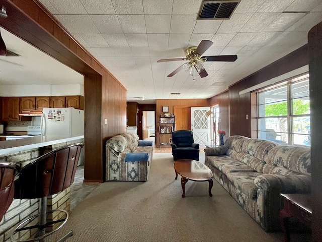 living room featuring ceiling fan, wood walls, and light carpet