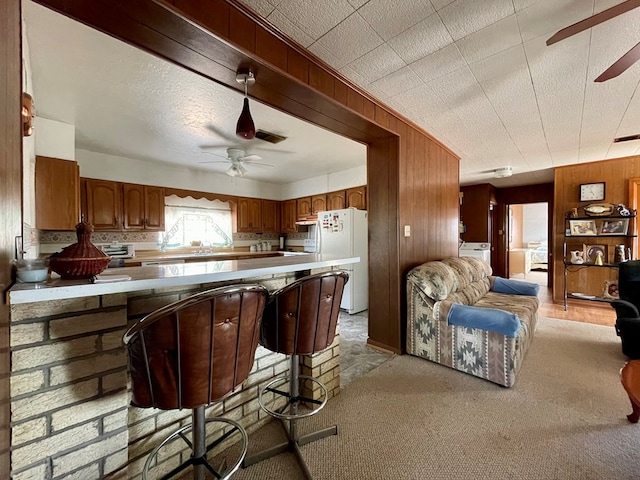 kitchen with sink, wooden walls, white fridge, a textured ceiling, and light carpet