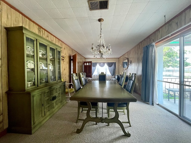 carpeted dining space featuring wooden walls, crown molding, and a notable chandelier