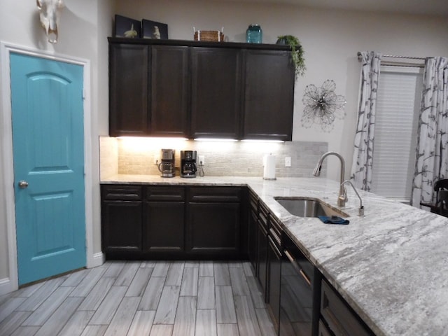 kitchen with decorative backsplash, kitchen peninsula, light stone countertops, sink, and light hardwood / wood-style flooring