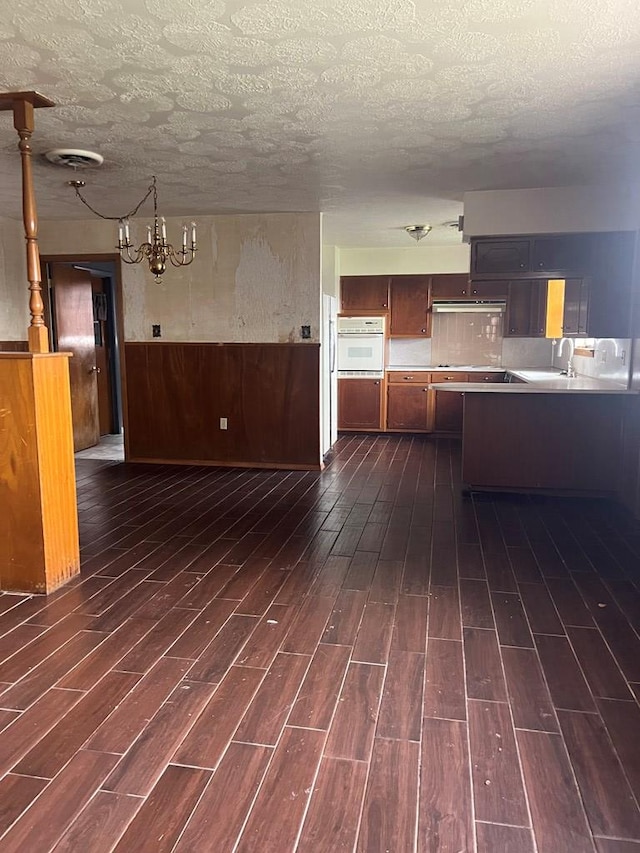 3805 E Everglade Ave, Odessa, TX 79762 - kitchen with white oven, dark wood-type flooring, a chandelier, under cabinet range hood, and a textured ceiling