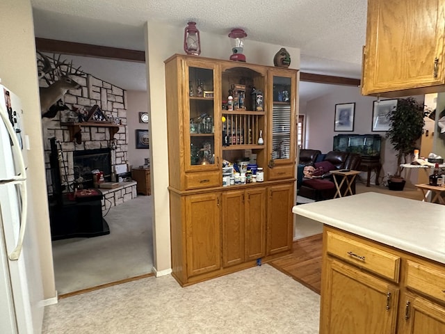 kitchen with a textured ceiling, light colored carpet, vaulted ceiling, and a stone fireplace