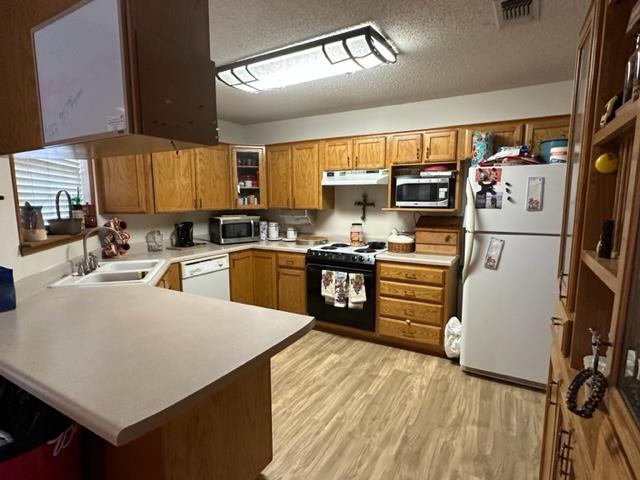 kitchen featuring kitchen peninsula, a textured ceiling, white appliances, sink, and light hardwood / wood-style floors