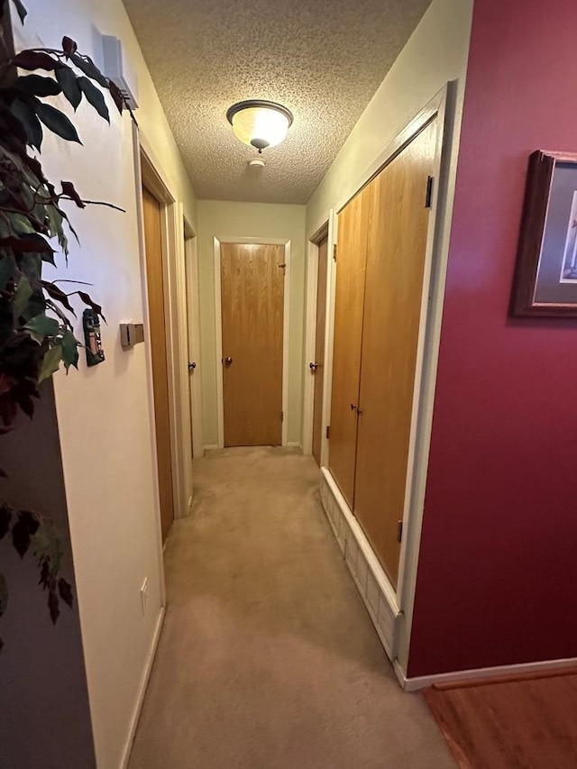 hall with a textured ceiling and light colored carpet