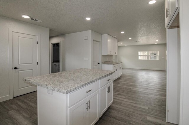 607 NW 11th St, Andrews, TX 79714 - kitchen featuring a textured ceiling, dark wood-style floors, light countertops, white cabinetry, and a center island