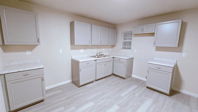 kitchen featuring baseboards, light countertops, a sink, and light wood finished floors