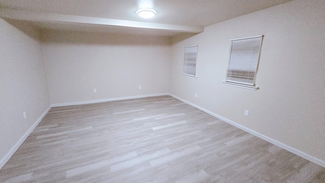 spare room with light wood finished floors, baseboards, and beamed ceiling