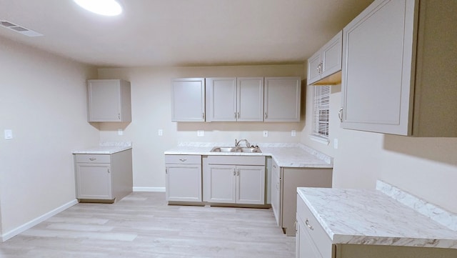 kitchen with light countertops, gray cabinetry, a sink, light wood-type flooring, and baseboards