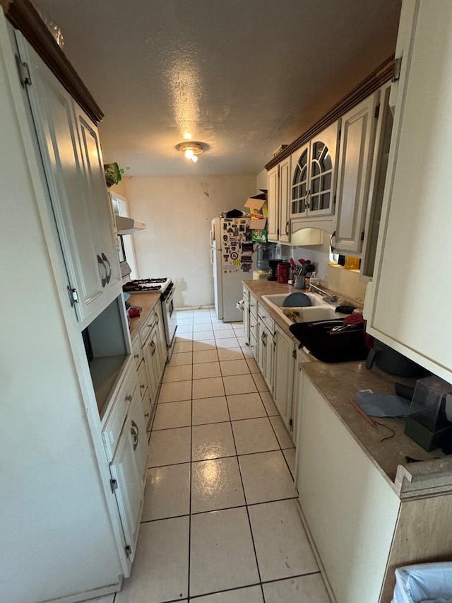 1044 Washington St, Kermit, TX 79745 - kitchen featuring a sink, white range with gas cooktop, light tile patterned floors, wall chimney range hood, and glass insert cabinets