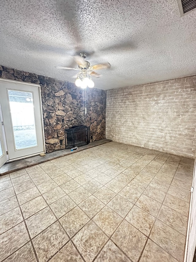 unfurnished living room with a fireplace, ceiling fan, and a textured ceiling