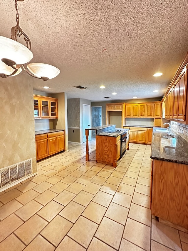 kitchen featuring light tile patterned flooring, dark stone counters, sink, a textured ceiling, and a kitchen island