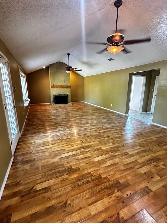 unfurnished living room with lofted ceiling, hardwood / wood-style flooring, ceiling fan, a textured ceiling, and a large fireplace