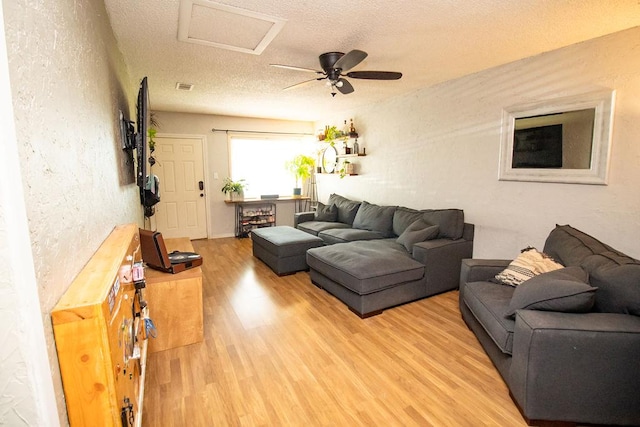 living room featuring ceiling fan, attic access, a textured ceiling, light wood-type flooring, and a textured wall