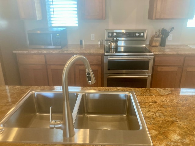 420 Santana Dr, Lajitas, TX 79852 - kitchen featuring appliances with stainless steel finishes, a sink, light stone counters, and brown cabinetry