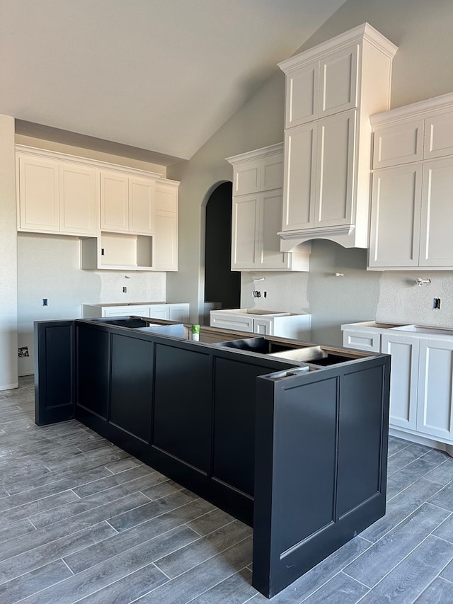 kitchen featuring a center island, vaulted ceiling, arched walkways, wood finish floors, and white cabinets