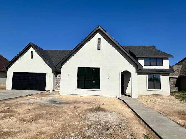 view of front facade featuring stucco siding, driveway, an attached garage, and roof with shingles