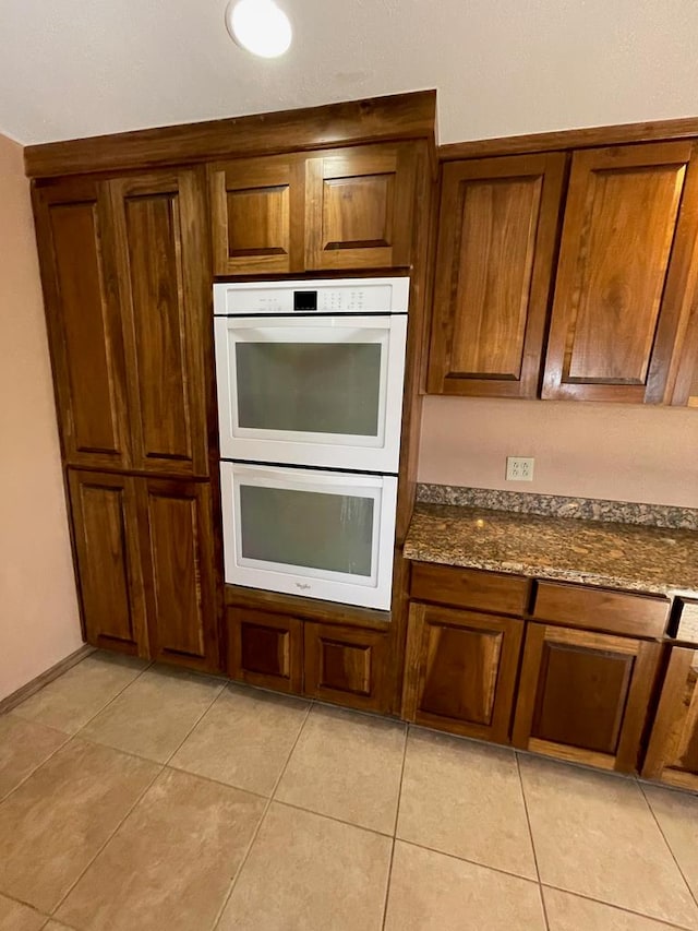 kitchen featuring double oven, dark stone counters, and light tile patterned flooring