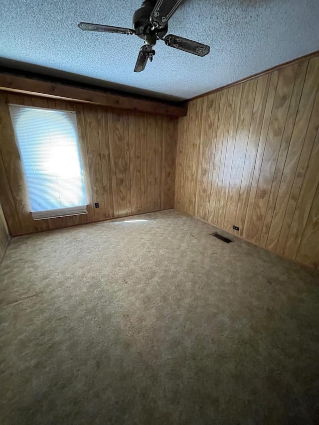 empty room featuring ceiling fan, a textured ceiling, carpet floors, and wooden walls