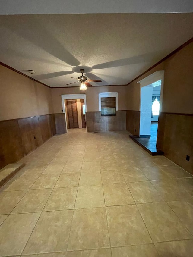 empty room with a textured ceiling, ceiling fan, ornamental molding, and light tile patterned flooring