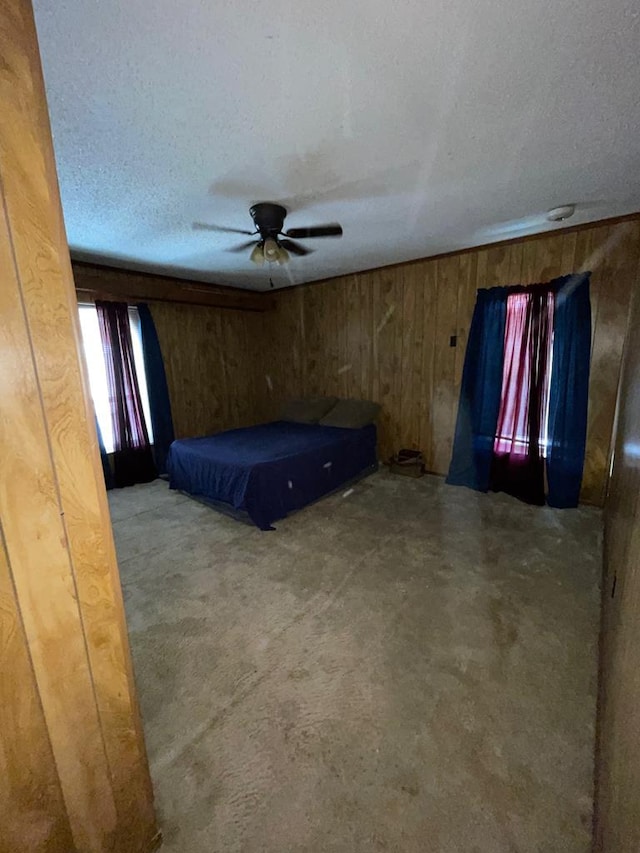 unfurnished bedroom with carpet flooring, a textured ceiling, ceiling fan, and wood walls