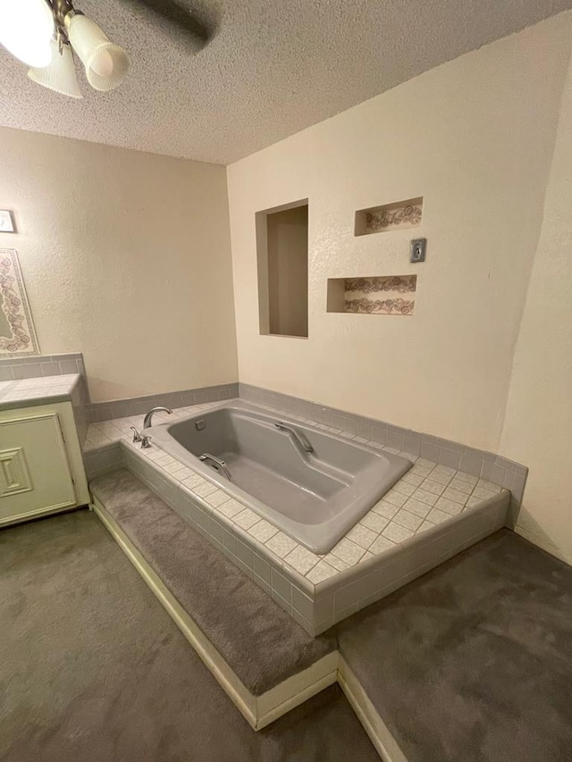 bathroom featuring a textured ceiling, tiled tub, and vanity