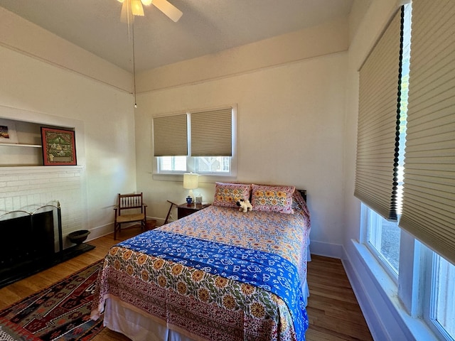 bedroom with ceiling fan, hardwood / wood-style floors, and a brick fireplace