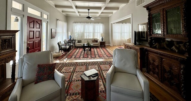 living area featuring ceiling fan, beamed ceiling, wood-type flooring, and coffered ceiling