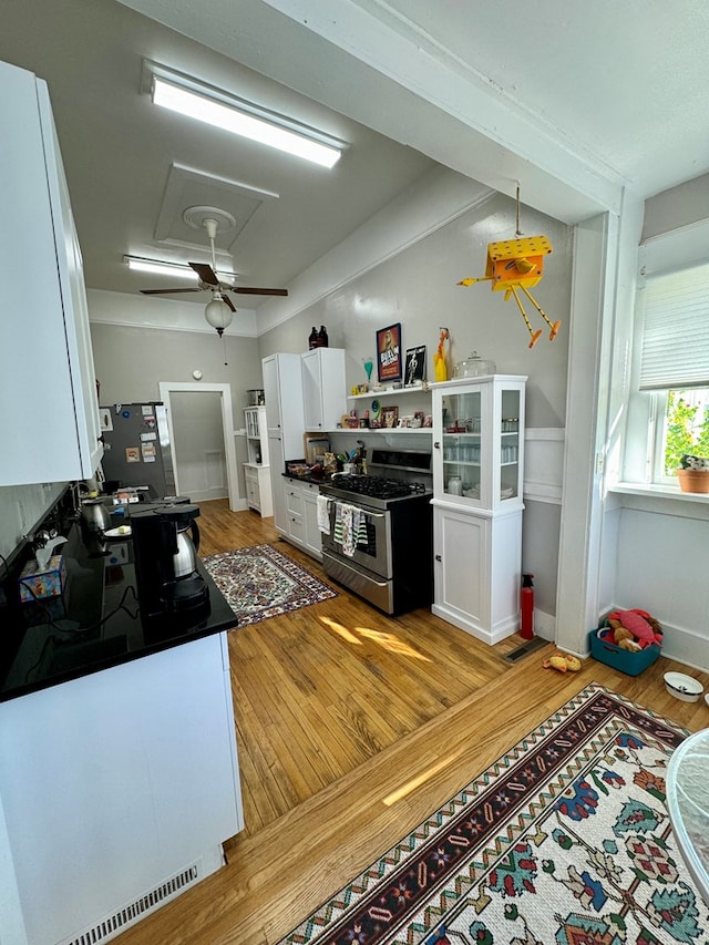 kitchen featuring ceiling fan, gas stove, wood-type flooring, and white cabinetry