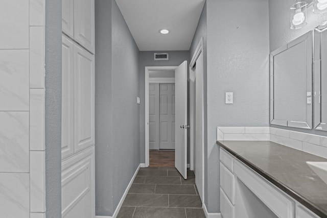 hallway featuring dark tile patterned floors, a textured wall, visible vents, and baseboards