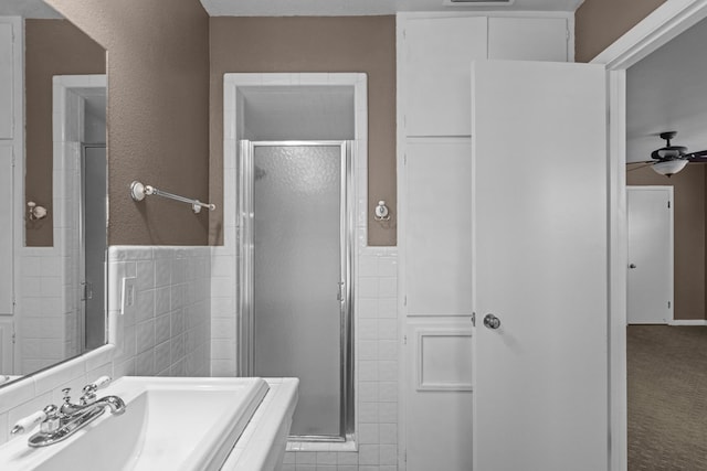 full bathroom featuring ceiling fan, tile walls, wainscoting, a stall shower, and a sink
