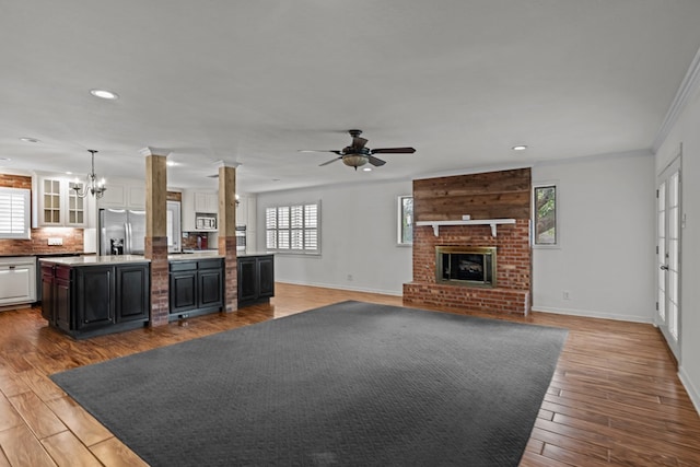 unfurnished living room featuring a brick fireplace, ceiling fan with notable chandelier, recessed lighting, baseboards, and wood finished floors