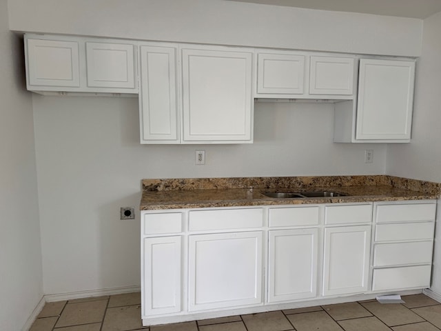 kitchen with white cabinetry, a sink, dark stone countertops, light tile patterned flooring, and baseboards