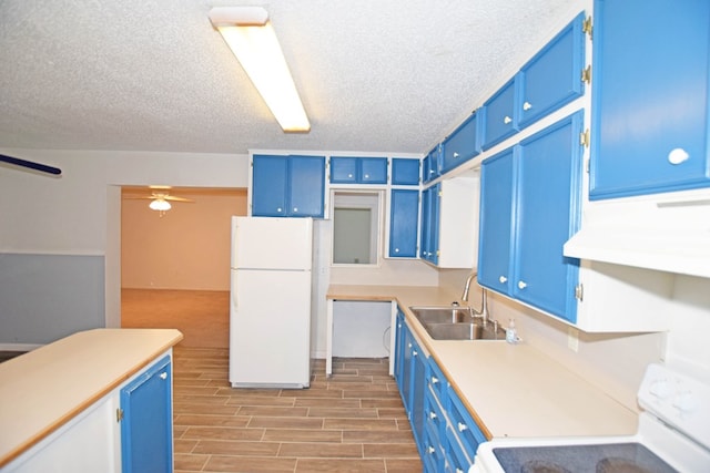 kitchen with blue cabinetry, white fridge, range, and sink