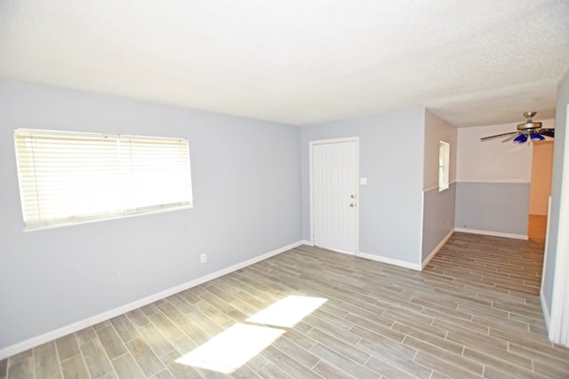 unfurnished room with a textured ceiling, light wood-type flooring, and ceiling fan